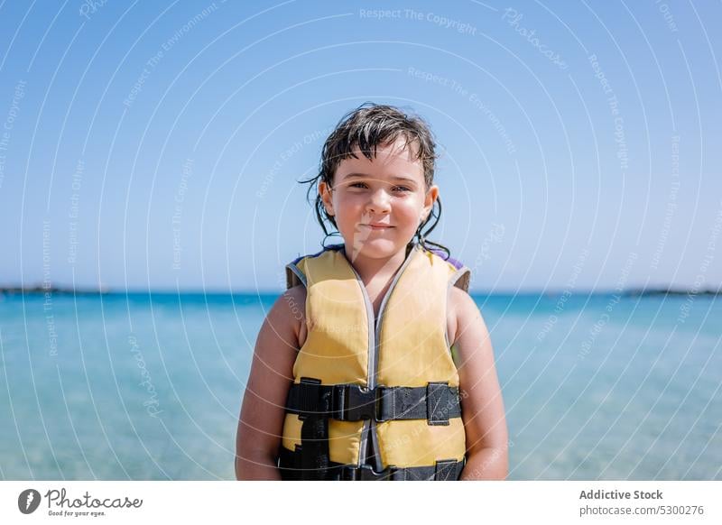 Lächelndes Mädchen in Sicherheits-Badejacke am Strand stehend Kind MEER Urlaub Sand Ufer positiv Meer Küste Tourist Sommer Feiertag Glück im Freien
