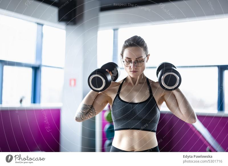 Junge Frau beim Training mit Hanteln in einem Fitnessstudio Wellness Wohlbefinden Bodybuilder sportlich Heben Bizeps Muskeln Curl-Hantel Bodybuilding Menschen