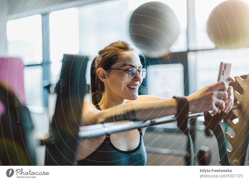Porträt einer jungen Frau, die in einer Turnhalle ein Mobiltelefon benutzt Wellness Wohlbefinden Bodybuilder sportlich Heben Bizeps Muskeln Curl-Hantel