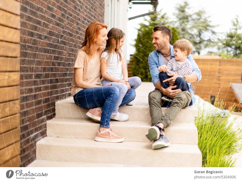Familie mit Mutter, Vater, Sohn und Tochter sitzt draußen auf den Stufen einer Veranda eines Backsteinhauses Eltern Treppe Mädchen Kind Fröhlichkeit Kindheit