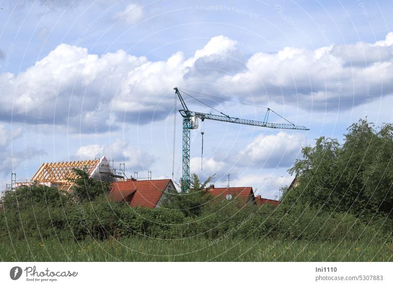 MainFux |Baukran im Wohngebiet Landschaft in Flußnähe Hausdächer Bauen Handwerk Rohbau Dachsparren Gerüst Wiese Sträucher Bäume Himmel Wolkenband