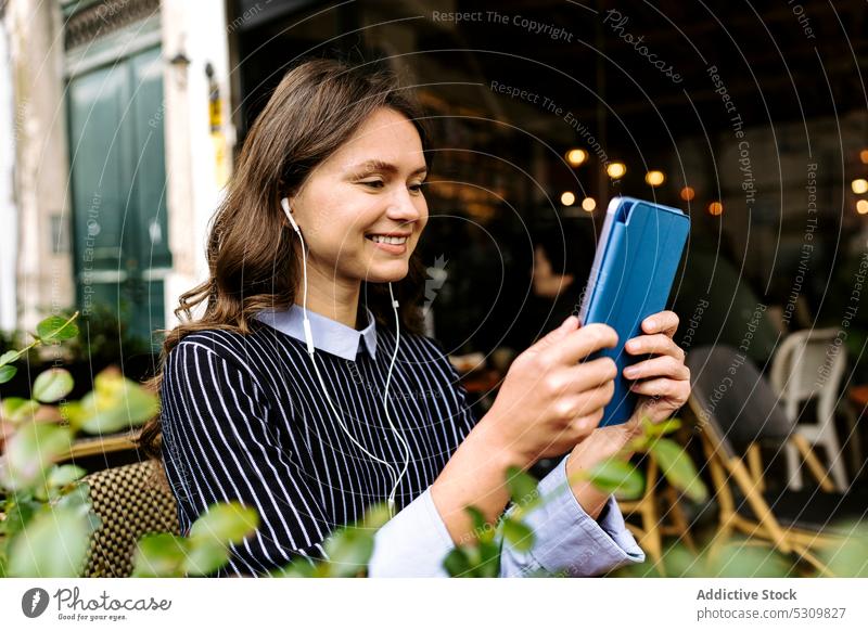 Frau mit Tablet auf der Terrasse eines Cafés positiv Tablette Kopfhörer zuschauen benutzend Lebensmittel Tee Teekanne Croissant online Internet Gerät Apparatur