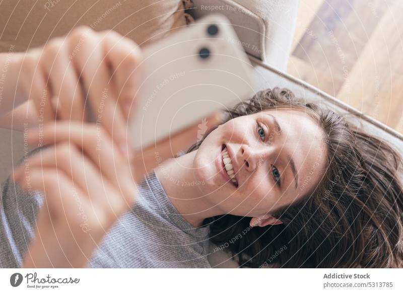 Lächelnde Frau, die auf dem Sofa ihr Smartphone durchsucht benutzend Surfen Lügen Glück Browsen heiter Internet Mobile heimwärts Apparatur Telefon online