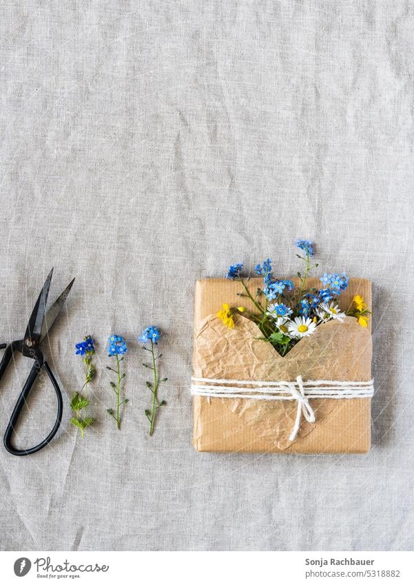 Ein in braunes Papier verpacktes Geschenk mit frischen Blumen nachhaltig Umwelt Geburtstag herzförmig Liebe Schere plastikfrei Packpapier Valentinstag Muttertag