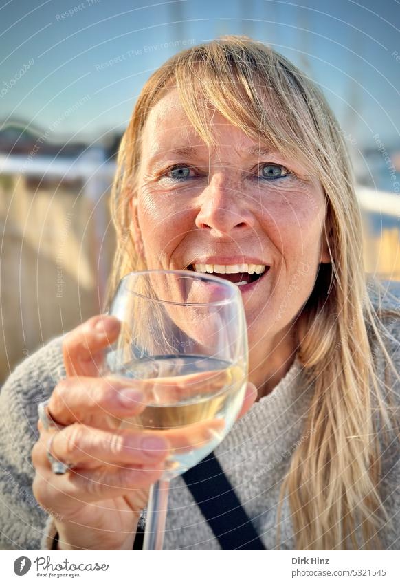 Lachende blonde Frau mit einem Glas Weißwein in der Hand Porträt Mensch Blick Blick in die Kamera Außenaufnahme Erwachsene Blick nach vorn Farbfoto Oberkörper