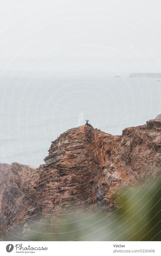 Ein abenteuerlustiger Mann steht am Rande einer Klippe und genießt die Aussicht auf die Atlantikküste in der Region Odemira im Südwesten Portugals. Wanderung durch die Rota Vicentina