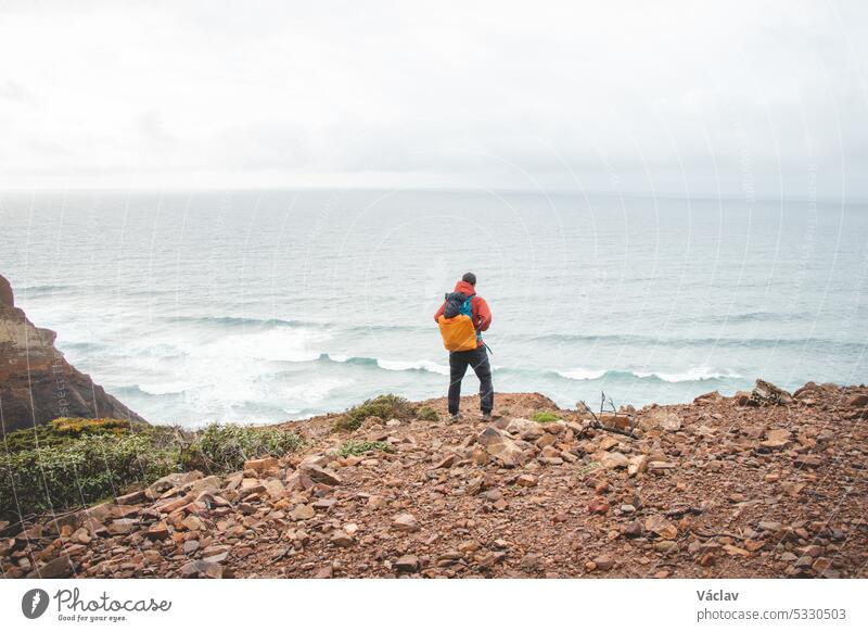 Ein abenteuerlustiger Mann steht am Rande einer Klippe und genießt die Aussicht auf die Atlantikküste in der Region Odemira im Südwesten Portugals. Wanderung durch die Rota Vicentina