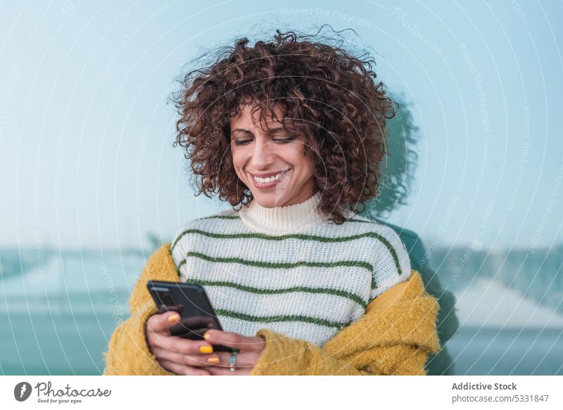 Positive Frau, die auf dem Boden auf der Straße auf ihrem Smartphone surft benutzend Lächeln Glück Nachricht heiter Browsen Apparatur Surfen Mobile Gerät lässig