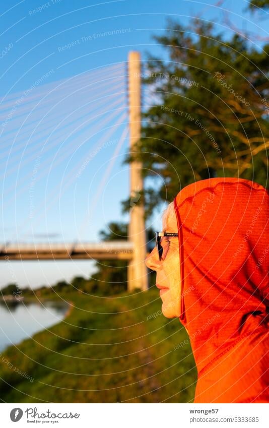 Portrait einer mit einer roten Kaputzenjacke bekleideten Frau am Ufer der Elbe bei Schönebeck rote Kapuzenjacke rote Jacke Profil Fluss linkes Flussufer Elbufer