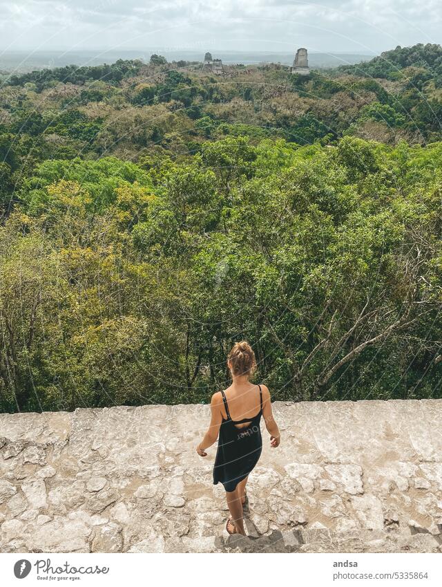 Frau blickt von oben auf einen Regenwald mit Tempeln Ausblick Urwald Dschungel Maya Antik Bauwerk historisch Archäologie von hinten Baumkrone Laubwald Laubwerk