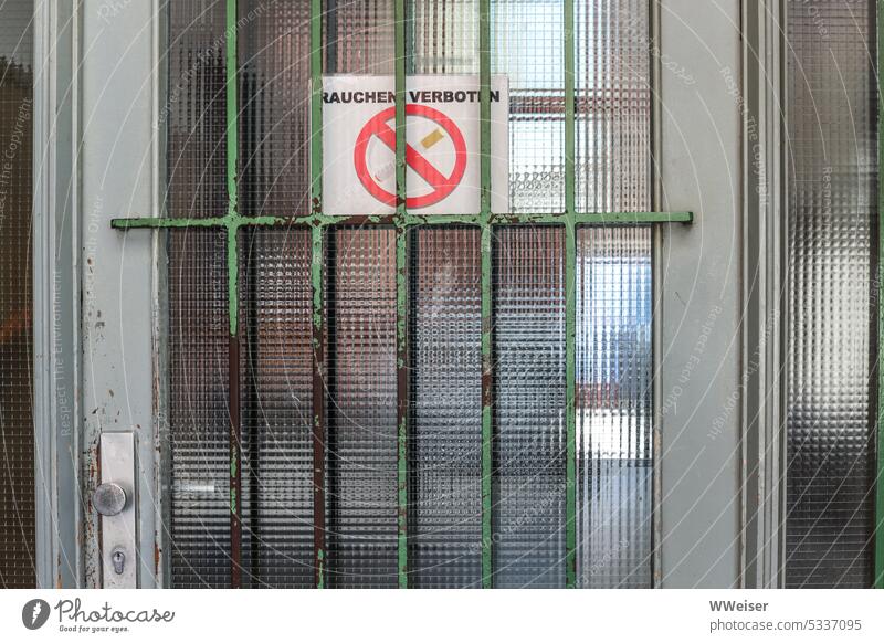 "Rauchen verboten" steht auf dem Zettel, der hinter dem Gitter der Haustür klebt Rauchverbot Verbot Verbotsschild Schild Warnung Tür Eingangstür Glas Stadt