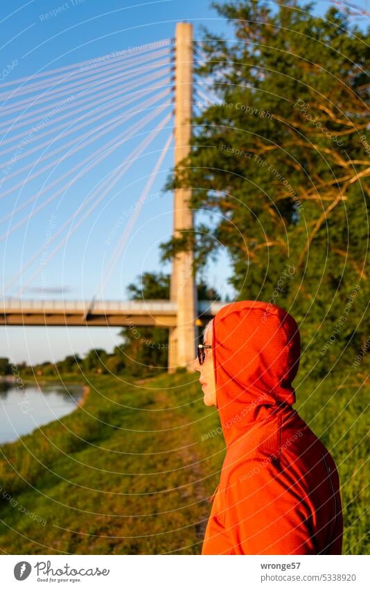 Eine mit einer roten Kaputzenjacke bekleidete Frau steht am linken Ufer der Elbe bei Schönebeck und schaut auf den Fluss rote Kapuzenjacke rote Jacke Profil