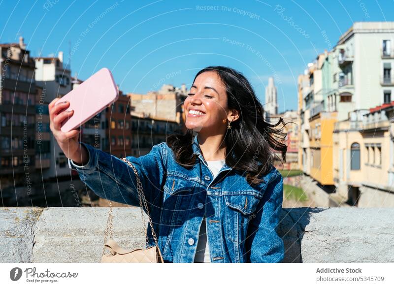 Lächelnde ethnische Frau steht auf dem Dach und macht ein Selfie Smartphone benutzend urban Gebäude Dachterrasse Begrenzung Wand jung Glück Mobile Telefon