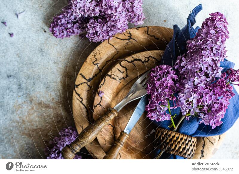 Frühlingstisch mit fliederfarbenen Blumen auf braunem Geschirr vor grauem Hintergrund Blütezeit Farbe farbenfroh Beton Besteck Abendessen Essgeschirr