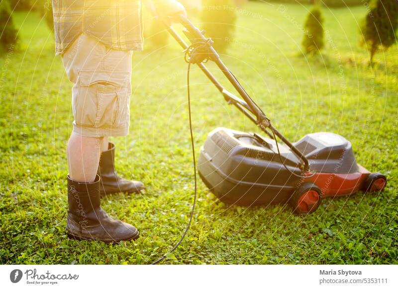 Älterer Mann Gärtner Schneiden von Gras in seinem Hinterhof mit Rasenmäher im Sommer sonnigen Tag. Rasenmähermaschine zum Trimmen von Gras. Saisonale Arbeiten im Garten.