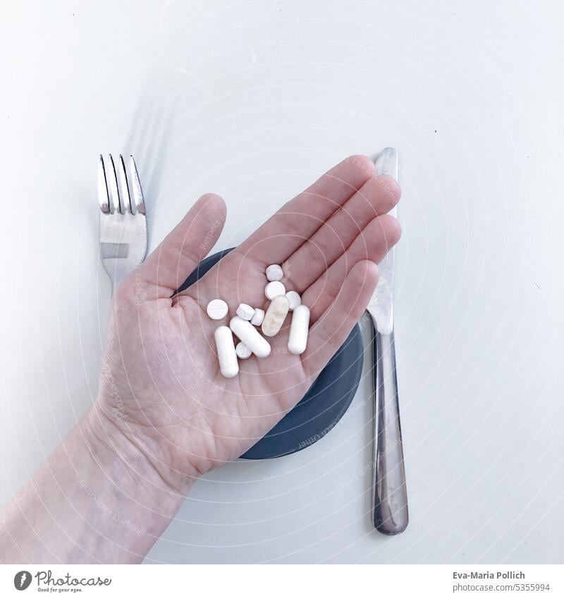 Eine Hand gefüllt mit Tabletten und Kapseln über einem Teller und Besteck Medikament Medikamente Medizin Krankheit Gesundheit Gesundheitswesen Verschreibung