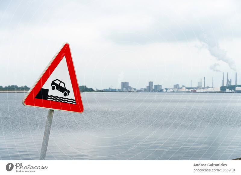 Verkehrsschild Achtung Ufer links im Bild, im Hintergrund defokussiert Wasser und Hafengebäude zu sehen, horizontal Warnschild Verkehrszeichen Uferbereich ufer
