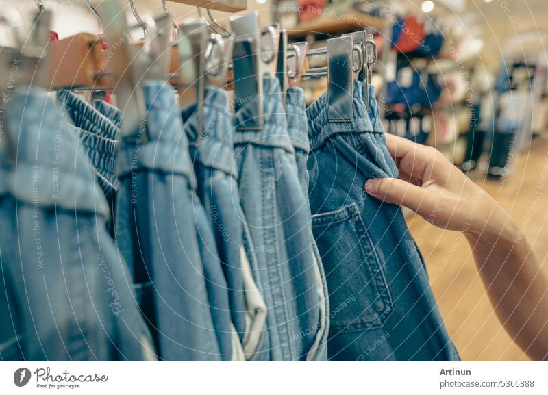 Frau kauft Jeanshosen in einem Bekleidungsgeschäft. Frau wählt Kleidung aus. Jeans auf Kleiderbügel hängen auf Rack in Bekleidungsgeschäft. Mode Einzelhandelsgeschäft im Einkaufszentrum. Kleidung auf Kleiderbügeln in einem Bekleidungsgeschäft.