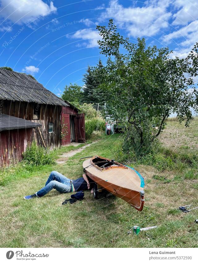 Mann repariert Klepper Faltboot Sommer Jeanshose Gras Natur Farbfoto Wiese Mensch Erholung Himmel liegen Landschaft blau Außenaufnahme Schuppen werkzeug