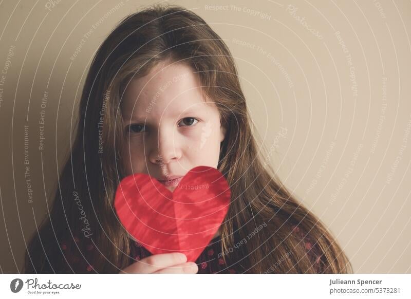 Junges Mädchen hält ein ausgeschnittenes farbiges Herz in der Hand heartshape Ausschnitt ausgeschnittenes Herz rotes Herz ausgeschnittene Herzform Kind achtsam