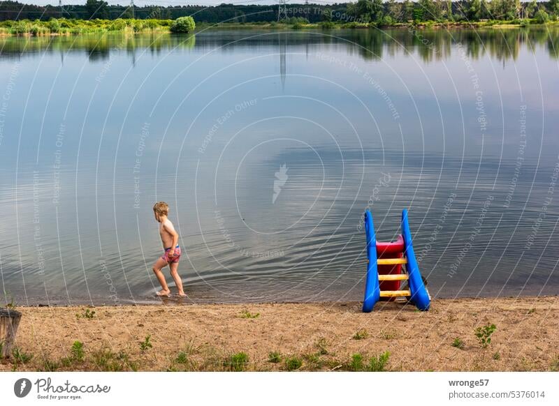 Zögerlich - Junge läuft am Rand eines Kiessees im flachen Wasser entlang Badesee Badestelle See Sommer Außenaufnahme Schwimmen & Baden Sommerurlaub