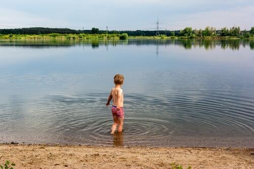 Junge steht im Wasser eines Kiessees und zögert noch etwas mit dem Baden Badesee Badestelle Rückansicht See Sommer Außenaufnahme Schwimmen & Baden Sommerurlaub