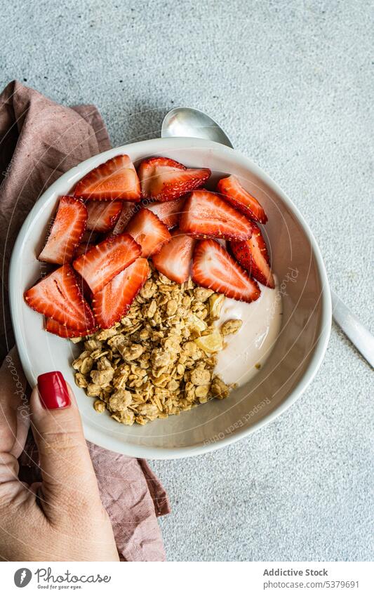 Abgeschnittene Hand hält Schüssel mit gesundem Frühstück mit Erdbeeren, Joghurt und Müsli Frau Beteiligung Hintergrund Beeren Schalen & Schüsseln Konzept Beton