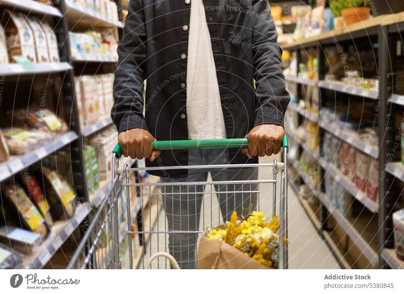 Unbekannter schwarzer Mann mit Einkaufswagen bei der Auswahl von Produkten anonym Supermarkt Kunde kaufen wählen Lebensmittelgeschäft Werkstatt Kauf Karre