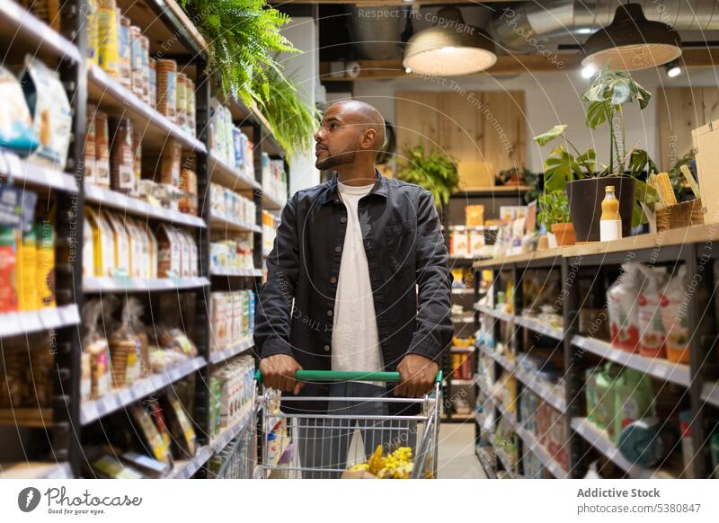 Schwarzer Mann mit Einkaufswagen bei der Produktauswahl Supermarkt Kunde kaufen wählen Lebensmittelgeschäft Werkstatt Kauf Karre Einkaufsmarkt Klient Laden