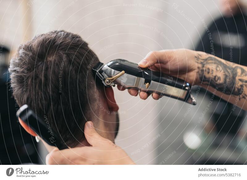 Anonymer junger Friseur, der mit einer Maschine im Friseursalon Haare schneidet Barbershop Vollbart bärtig Bartiger Mann Schönheit Pflege Klient Ausschnitt