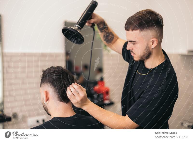 Junger Friseur kämmt Haare im Friseursalon Erwachsener Barbershop Vollbart Schönheit Business Pflege Freizeitkleidung Kaukasier Klient Frisur Trockner Gesicht