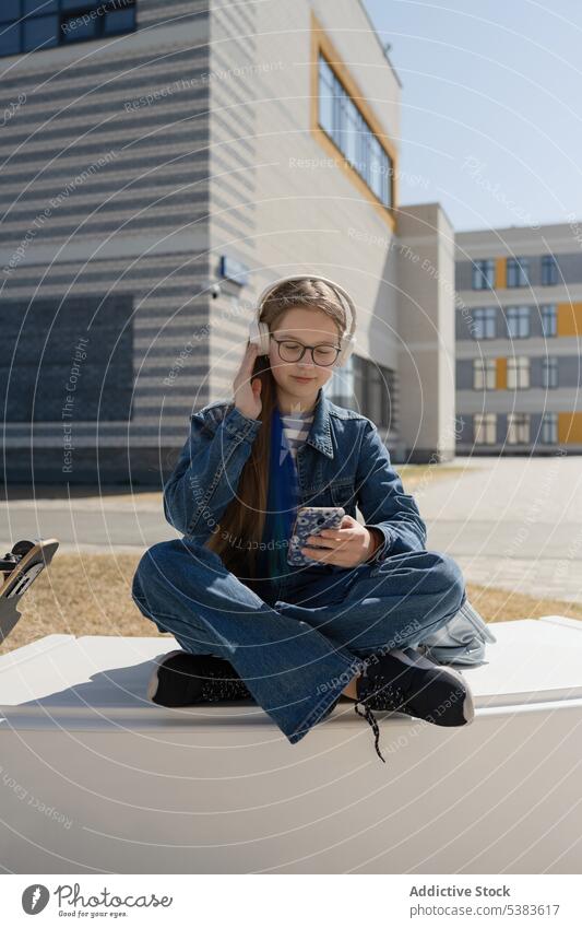 Trendiges Teenie-Mädchen genießt Musik auf einer Bank in der Stadt Kopfhörer zuhören Freizeit sorgenfrei genießen Teenager benutzend Großstadt modern Stil