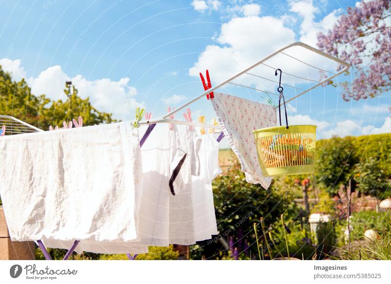 An einem sonnigen Tag steht ein Wäschetrockner auf der Terrasse zum Trocknen weißer Kleidung. Zusammenklappbarer Wäscheständer mit Wäscheklammerbeutel aus Kunststoff. Plastikkorb für Wäscheklammern. Platz zum Kopieren