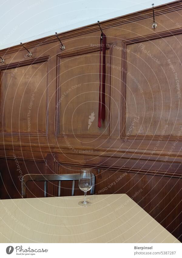 Eine an einem Kleiderhaken vergessene Krawatte und ein leeres Glas in einem Lokal Gastronomie Kneipe Mann Restaurant Schlips Stuhl Tisch Wand Holzwand