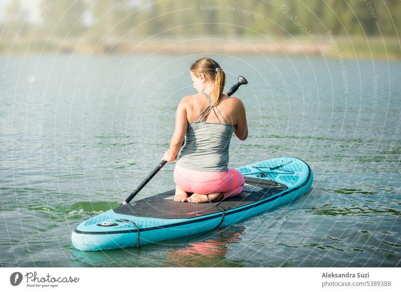 Junge, sportliche Frau paddelt auf dem Fluss und sitzt auf dem Surfbrett. aktiv Aktivität Abenteuer attraktiv Strand schön Holzplatte Boarding Kaukasier Übung