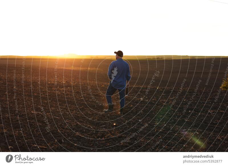 Agrarwirtschaft. Rückansicht eines männlichen Landwirts, der bei Sonnenuntergang im Frühling durch ein gepflügtes Feld geht. Besitzer landwirtschaftlichen Betrieb ist die Überprüfung und Prüfung Ackerland vor der Aussaat Landwirtschaft Pflanzen.