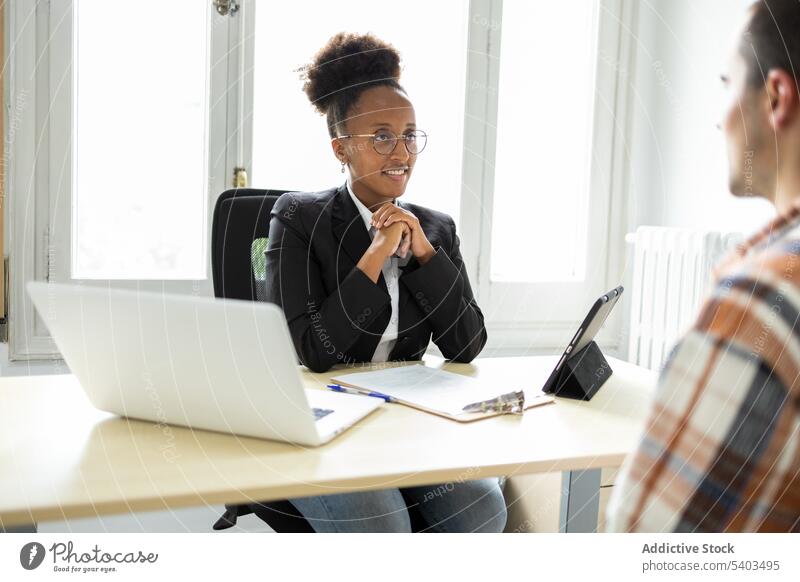 Fokussierte schwarze Rechtsberaterin im Gespräch mit einem Mandanten am Tisch Frau Anwalt Mann Klient diskutieren interagieren Arbeit professionell Lächeln Büro