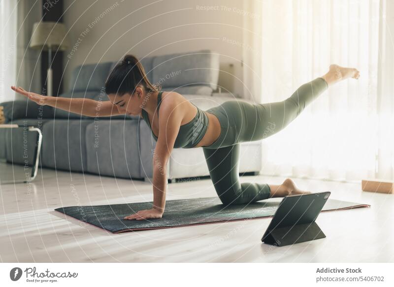 Flexible Frau in Vogelhund-Pose auf Matte zu Hause Sportlerin chakravakasana Asana Gleichgewicht Tablette Yoga online benutzend üben Appartement positionieren