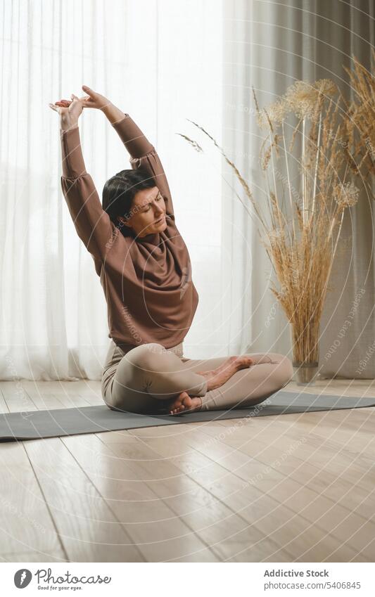 Ruhige Frau, die sich auf einer Matte in der Nähe eines Vorhangs zu Hause ausstreckt meditieren Yoga Zen üben Unterlage Windstille Barfuß Sportbekleidung