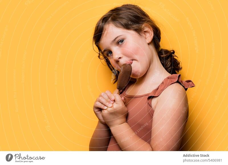 Hungriges Kind isst Eis in gelbem Studio Speiseeis lutschen Schokolade süß lecker Sommer Urlaub Porträt Mädchen essen Dessert Kindheit Badeanzug brünett