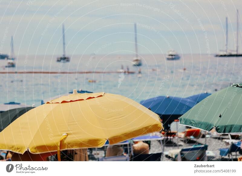 Sonnenschirme in gelb, blau und grün, dahinter das Meer, an der Küste der italienischen Riviera Ligurien Stand Wasser Boote Baden Sonnenbad Urlaub sonnig schön