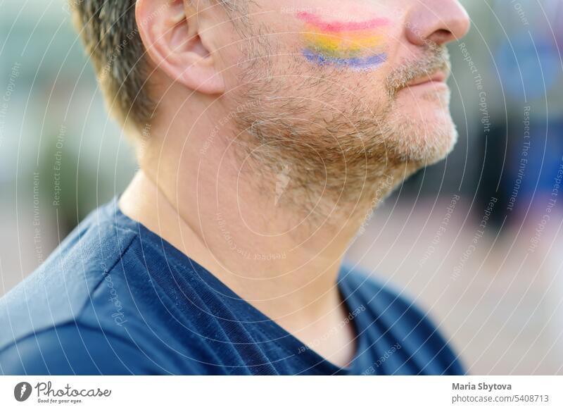 Nahaufnahme von Gesicht Mann Aktivist mit Malerei Regenbogen auf der Wange während LGBT Pride Event. Kämpfen für die Gleichheit der Rechte von sexuellen Minderheiten.