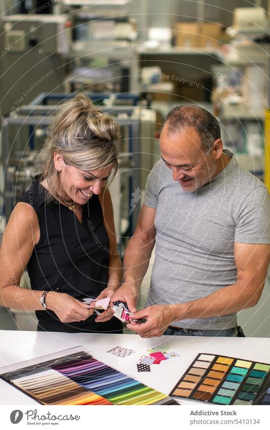 Glücklicher Mann mittleren Alters und erwachsene Frau, die bunte Stoffmuster im Tageslicht untersuchen Probe Lächeln Herstellung Fabrik Qualität Textil prüfen