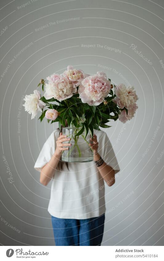 Unerkanntes Kind im Vorschulalter mit blühenden Pfingstrosen in einem Glasgefäß frisch Blütezeit Blume grün Blatt Vorbau einrichten geblümt Kleid Stil Vase