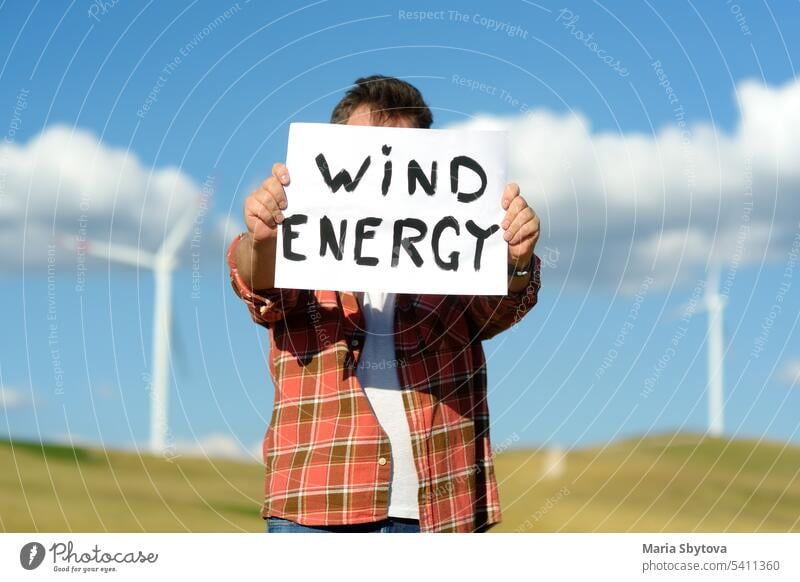Umweltaktivist mit Banner "Windenergie" vor dem Hintergrund von Kraftwerken für erneuerbare Energieerzeugung. Person und Windmühlen. Windturbinen zur Stromerzeugung. Grün