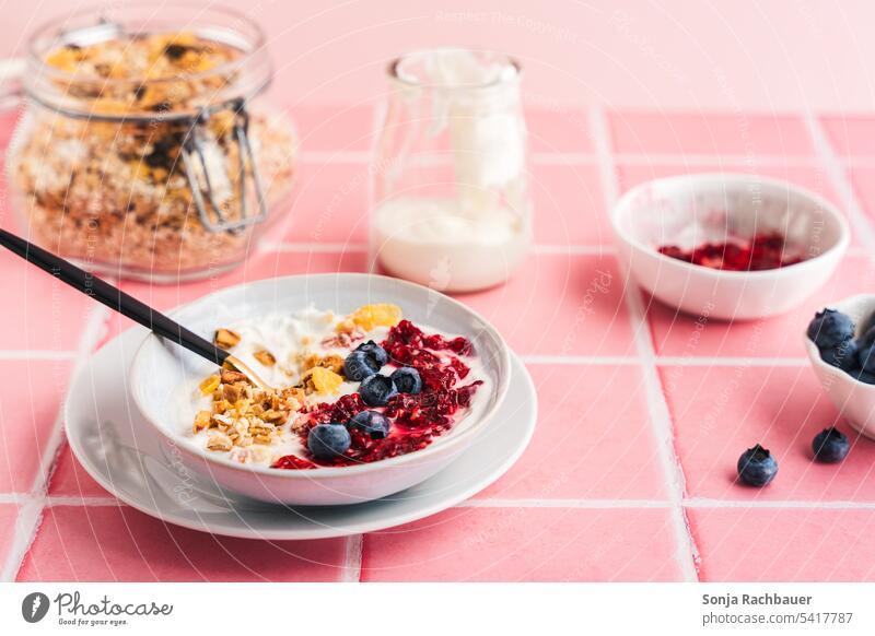 Granola, frische Beeren und Joghurt in einer Schüssel auf rosa Kacheln. Frühstück. Lebensmittel Diät Müsli lecker Morgen Himbeeren Heidelbeere Zutaten süß