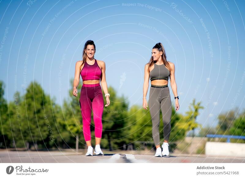 Fröhliche sportliche Zwillinge auf Asphalt stehend Start rennen joggen laufen passen Fitness Training Frauen Pferdeschwanz Schwester Zusammensein heiter positiv