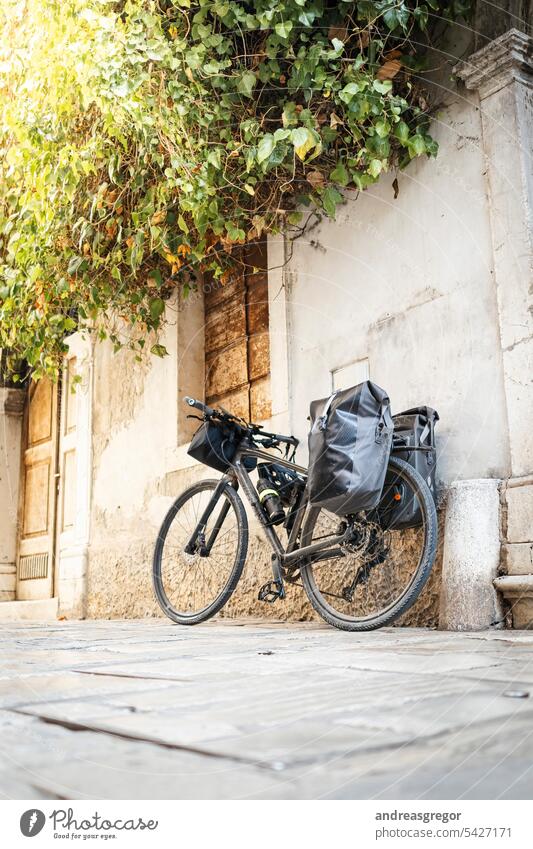 Fahrrad mit bepackten Taschen lehnt an einer Häuserwand in einer Gasse in einem südeuropäischen Städtchen Fahrradreise Fahrradtour Fahrradfahren Bikepacking