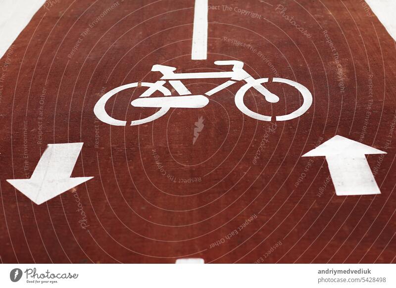 Neue Kennzeichnung Fahrradweg. Weißes Fahrrad-Symbol und zwei entgegengesetzte Pfeile auf rotem Asphalt Fahrbahn, Straße. Fahrradweg in der Stadt. Zwei-Wege-Fahrradweg auf einer Allee. Lebensstil. Stadtverkehr und Transport