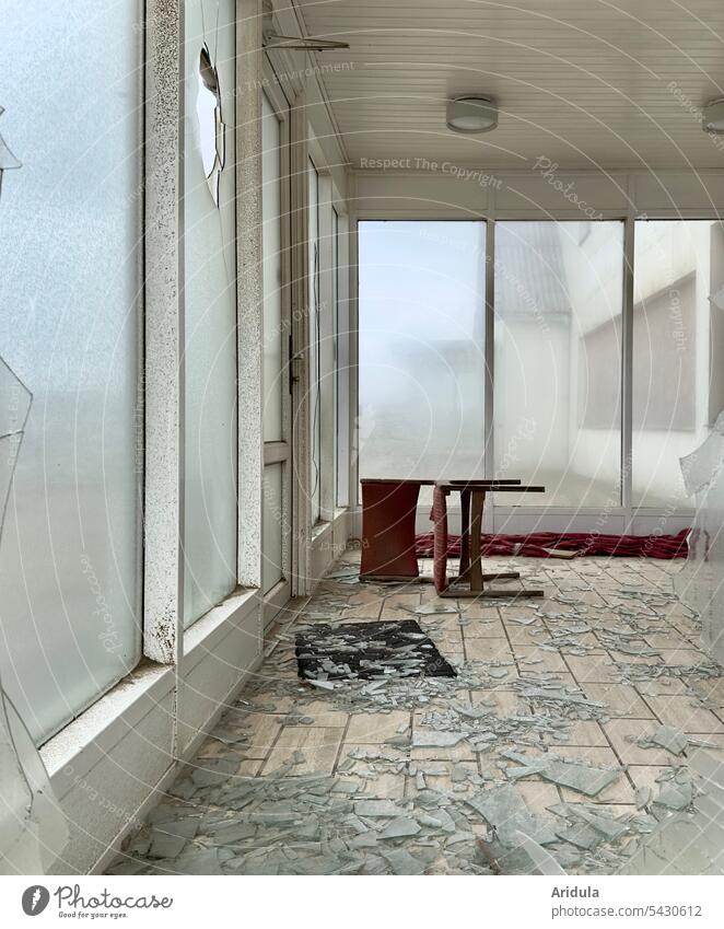 Lost place | Ein dunkelroter Stuhl liegt auf dem Boden in einem verlassenen Raum mit tiefen Fenstern. Einige Fenster sind kaputt. Glasscherben liegen auf dem Boden.